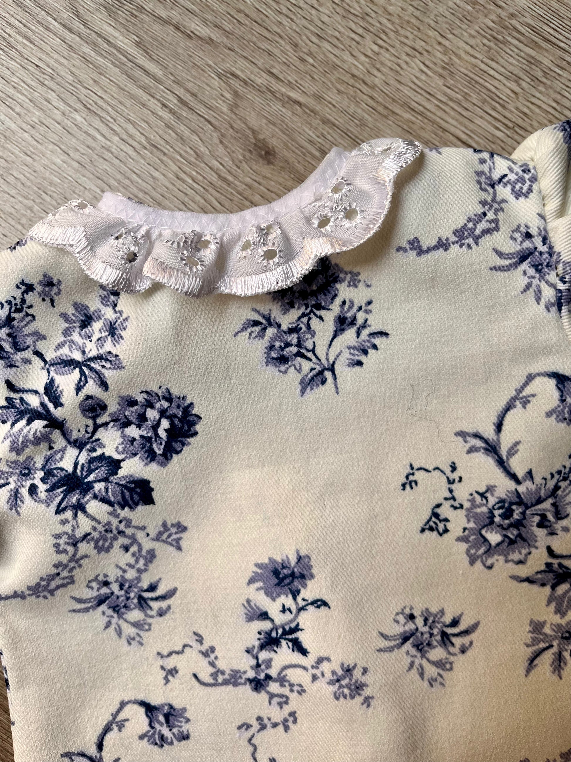 Close up of a floral patterned dolls dress with lace trim.